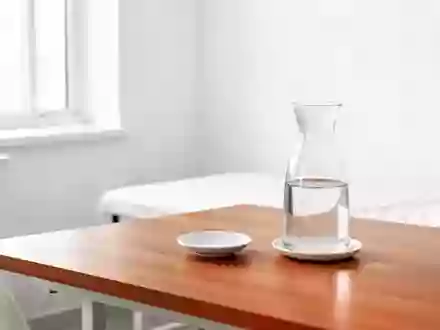 Ein minimalistisch eingerichteter, heller Behandlungsraum mit einer Wasserkaraffe und einer Untertasse auf einem Holztisch. - Foto: über boerse-global.de