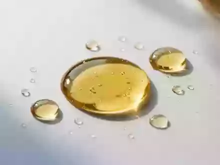 Goldene Öltröpfchen auf einer sauberen, weißen Laboroberfläche bei sanftem Tageslicht. - Foto: über boerse-global.de