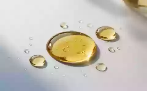 Goldene Öltröpfchen auf einer sauberen, weißen Laboroberfläche bei sanftem Tageslicht. - Foto: über boerse-global.de