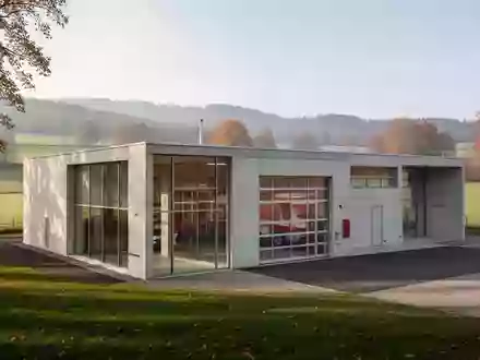 Modernes Feuerwehrgerätehaus aus Beton und Glas in einer ländlichen Umgebung bei Tageslicht. - Foto: über boerse-global.de