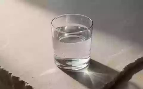 Ein klares Glas Wasser auf einer schlichten Steinoberfläche bei natürlichem Licht, das Ruhe und biologische Prozesse symbolisiert. - Foto: über boerse-global.de