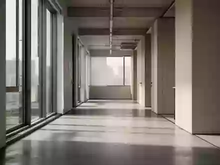 Ein minimalistischer, leerer Büroflur mit weichem Tageslichteinfall und architektonischen Schatten auf dem Boden. - Foto: über boerse-global.de