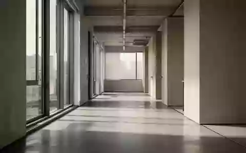 Ein minimalistischer, leerer Büroflur mit weichem Tageslichteinfall und architektonischen Schatten auf dem Boden. - Foto: über boerse-global.de