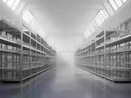Ein minimalistisches, menschenleeres Logistiklager mit leeren Stahlregalen und poliertem Betonboden bei natürlichem Tageslicht. - Foto: über boerse-global.de