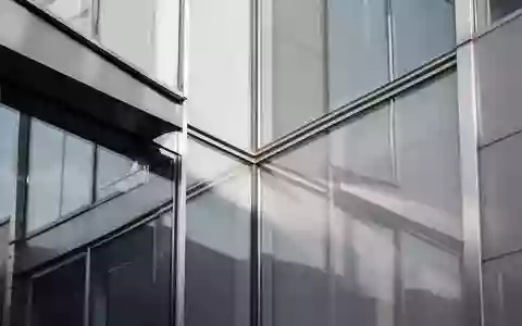 Moderne architektonische Fassade aus Glas und Stahl mit Fokus auf geometrische Linien und Lichtreflexionen. - Foto: über boerse-global.de