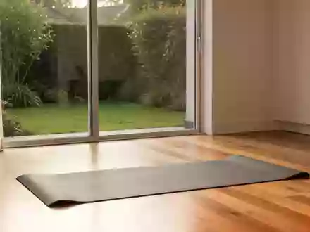 Eine leere Yogamatte auf einem Holzboden in einem hellen, von Tageslicht durchfluteten Raum mit Blick in einen Garten. - Foto: über boerse-global.de
