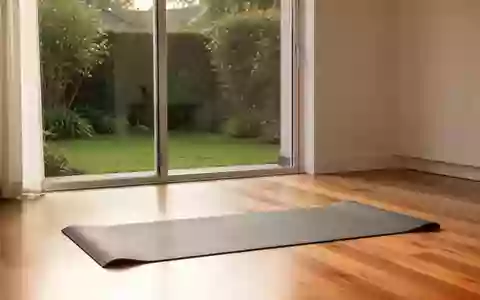 Eine leere Yogamatte auf einem Holzboden in einem hellen, von Tageslicht durchfluteten Raum mit Blick in einen Garten. - Foto: über boerse-global.de