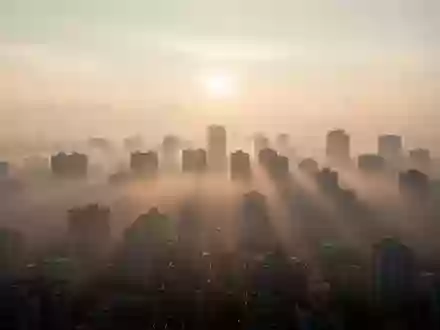 Dunstige Stadtlandschaft bei Sonnenaufgang mit sichtbarer Luftverschmutzung über den Dächern. - Foto: über boerse-global.de