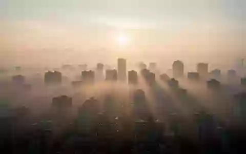 Dunstige Stadtlandschaft bei Sonnenaufgang mit sichtbarer Luftverschmutzung über den Dächern. - Foto: über boerse-global.de