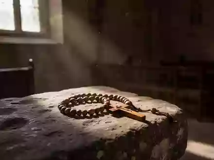 Ein hölzerner Rosenkranz liegt auf einem steinernen Untergrund in einem sonnendurchfluteten, ruhigen Kirchenraum. - Foto: über boerse-global.de