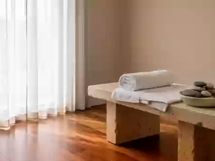 Ein minimalistisch gestalteter Wellnessraum mit einem sauberen Holzboden, einer zusammengerollten Baumwollhandtuchrolle und glatten Kieselsteinen auf einer Steinbank. - Foto: über boerse-global.de