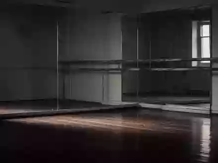 Ein leerer Ballettsaal mit einer hölzernen Ballettstange und einem großen Spiegel in gedämpftem Licht. - Foto: über boerse-global.de