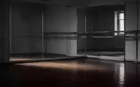 Ein leerer Ballettsaal mit einer hölzernen Ballettstange und einem großen Spiegel in gedämpftem Licht. - Foto: über boerse-global.de