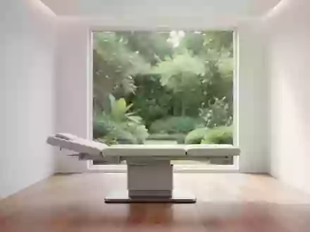 Ein minimalistischer, heller medizinischer Untersuchungsraum mit weichem Tageslicht und Blick in einen grünen Garten. - Foto: über boerse-global.de