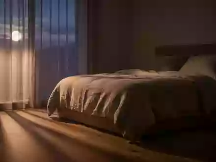 Ein minimalistisch eingerichtetes, ruhig beleuchtetes Schlafzimmer in der Abenddämmerung mit weicher Bettwäsche. - Foto: über boerse-global.de