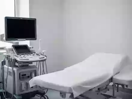 Ein klinischer Untersuchungsraum mit einem modernen Ultraschallgerät und einer leeren Untersuchungsliege in hellem, natürlichem Licht. - Foto: über boerse-global.de