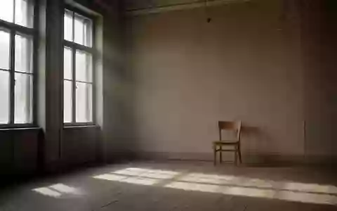 Ein minimalistischer, leerer Warteraum mit hohen Fenstern, schlichtem Holzstuhl und diffusem Tageslicht in einem Altbau. - Foto: über boerse-global.de