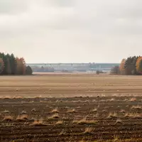 Weite, unberührte Ackerflächen im Mühlenbecker Land unter einem bewölkten Himmel, im Hintergrund schemenhaft eine Autobahntrasse. - Foto: über boerse-global.de