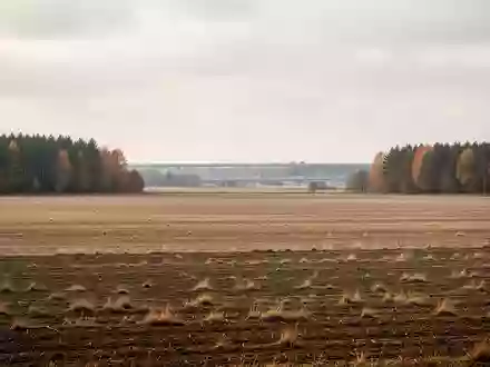 Weite, unberührte Ackerflächen im Mühlenbecker Land unter einem bewölkten Himmel, im Hintergrund schemenhaft eine Autobahntrasse. - Foto: über boerse-global.de