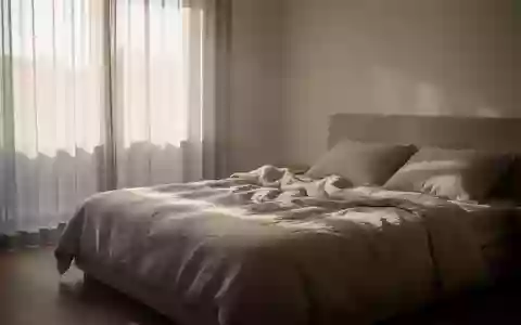 Ein minimalistisch eingerichtetes Schlafzimmer mit weichem Tageslicht, das auf ein ungemachtes Bett fällt. - Foto: über boerse-global.de