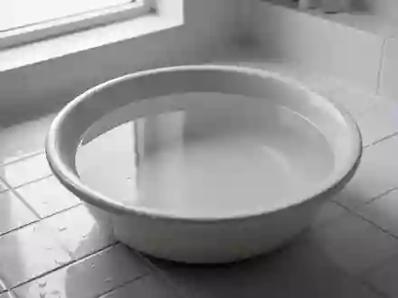 Eine leere, mit Wasser gefüllte Keramikschale auf einem weißen Fliesenboden in einem minimalistischen Badezimmer. - Foto: über boerse-global.de