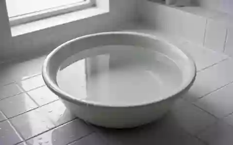 Eine leere, mit Wasser gefüllte Keramikschale auf einem weißen Fliesenboden in einem minimalistischen Badezimmer. - Foto: über boerse-global.de