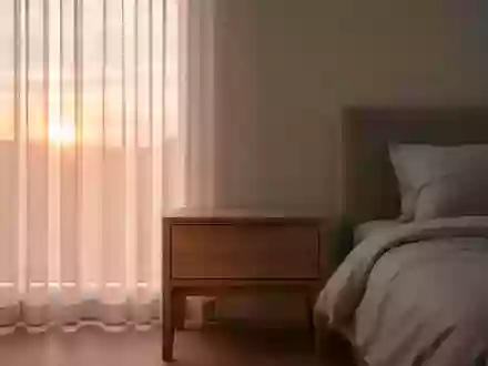 Ein minimalistisch eingerichtetes Schlafzimmer am Morgen mit weichem Tageslicht, das auf einen hölzernen Nachttisch fällt. - Foto: über boerse-global.de