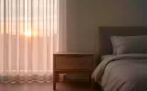 Ein minimalistisch eingerichtetes Schlafzimmer am Morgen mit weichem Tageslicht, das auf einen hölzernen Nachttisch fällt. - Foto: über boerse-global.de