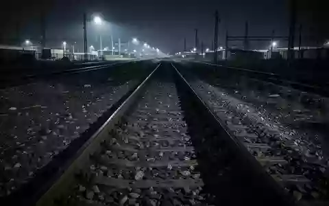 Leere Bahngleise bei Nacht mit Schotterbett und Stahlschienen in einer stimmungsvollen, menschenleeren Umgebung. - Foto: über boerse-global.de