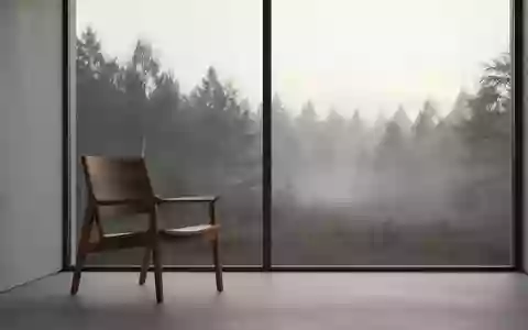 Ein minimalistischer, ruhiger Raum mit einem leeren Holzstuhl vor einem großen Fenster, das den Blick auf einen nebligen Wald freigibt. - Foto: über boerse-global.de