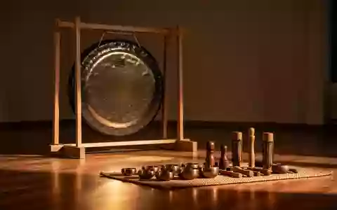 Ein meditativer Raum mit einem großen, verzierten Gong auf einem Holzständer und verschiedenen Klanginstrumenten auf einer Matte. - Foto: über boerse-global.de