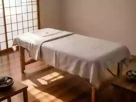 Ein minimalistischer, ruhiger Behandlungsraum für Massagen mit einem hölzernen Massagetisch und natürlichem Licht. - Foto: über boerse-global.de