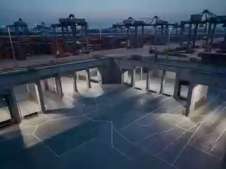 Ein leeres, industrielles Logistikzentrum mit verladenen Containern und geometrischen Schatten in der Abenddämmerung. - Foto: über boerse-global.de
