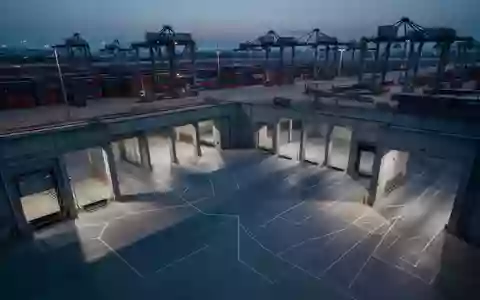 Ein leeres, industrielles Logistikzentrum mit verladenen Containern und geometrischen Schatten in der Abenddämmerung. - Foto: über boerse-global.de