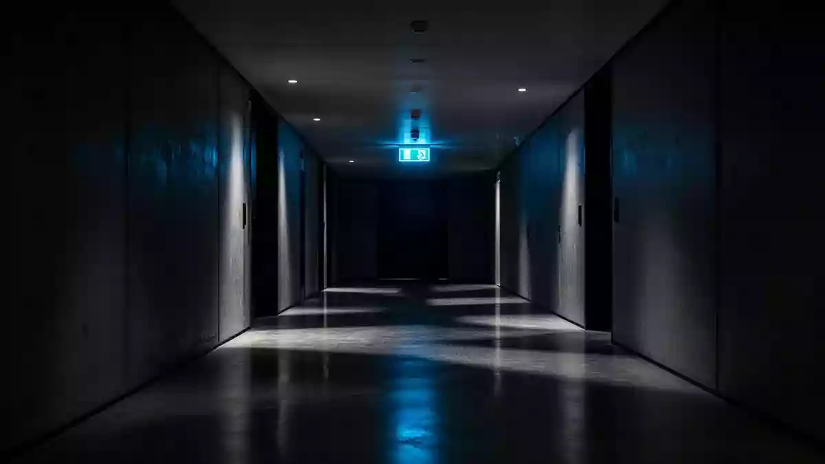 Ein minimalistischer, schattiger Flur mit einem blauen Notausgangsschild an der Wand. Illustration mit AI erstellt.