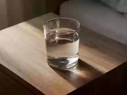 Ein Glas Wasser steht in sanftem Morgenlicht auf einem hölzernen Nachttisch. - Foto: über boerse-global.de
