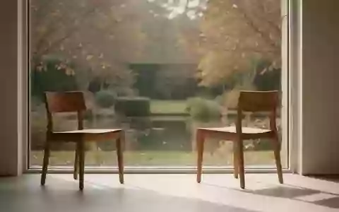 Ein minimalistisch eingerichteter Raum mit einem leeren Holzstuhl vor einem Fenster mit Blick in einen ruhigen Garten. - Foto: über boerse-global.de