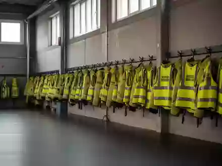 Leere Ausbildungshalle einer Feuerwehr mit ordentlich aufgehängter Schutzausrüstung und reflektierenden Sicherheitswesten. - Foto: über boerse-global.de