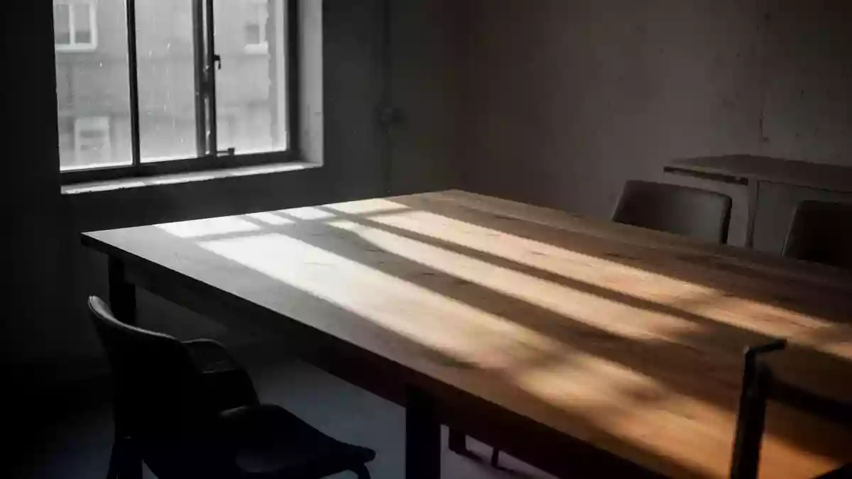 Ein minimalistischer, leerer Esstisch in natürlichem Morgenlicht mit langen Schatten auf einer Holzoberfläche. Illustration mit AI erstellt.