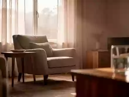 Ein ruhig beleuchtetes Wohnzimmer mit einem bequemen Sessel am Fenster und einer friedlichen, leeren Atmosphäre. - Foto: über boerse-global.de