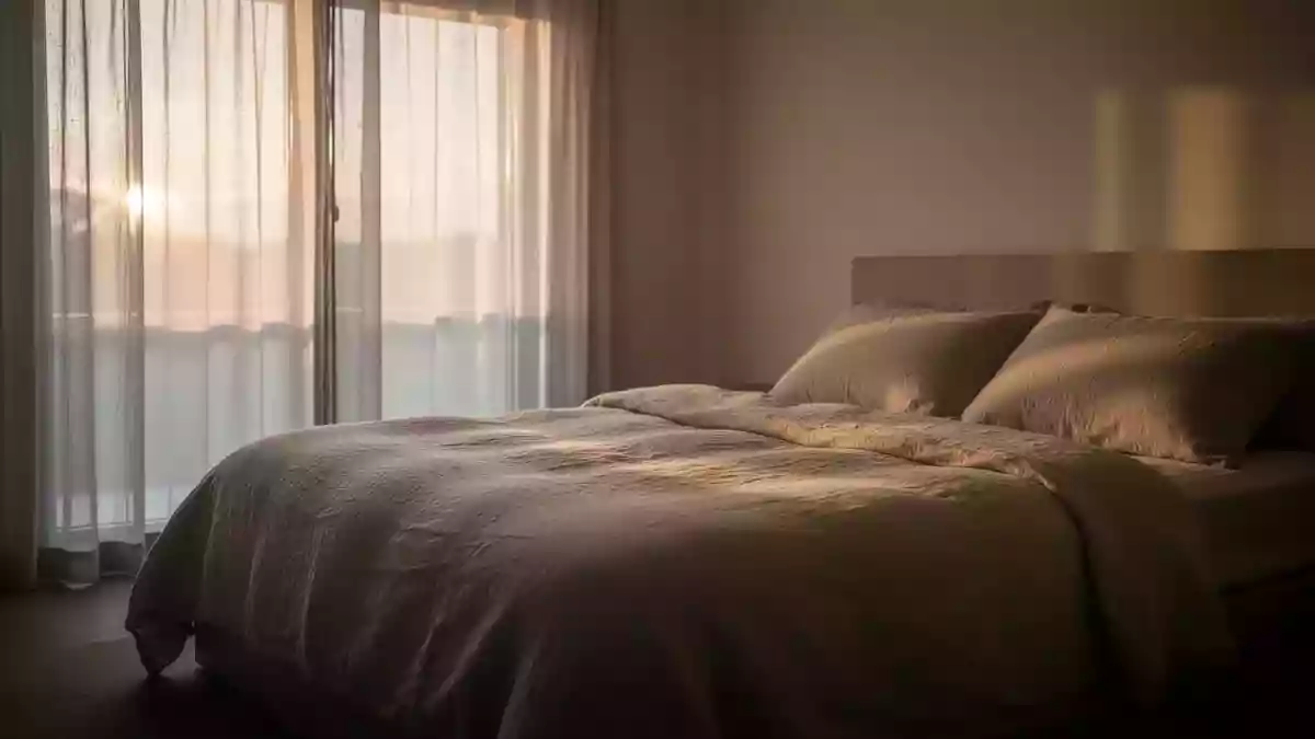 Ein minimalistisch eingerichtetes Schlafzimmer in den frühen Morgenstunden mit sanftem, natürlichem Licht. Illustration mit AI erstellt.