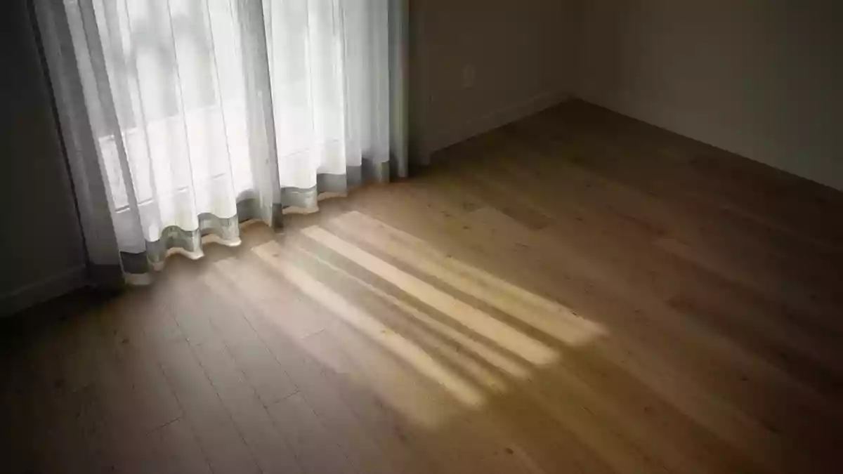 Ein ruhiger, minimalistischer Raum mit sanftem, natürlichem Licht, das durch einen Vorhang auf einen Holzboden fällt. Illustration mit AI erstellt.