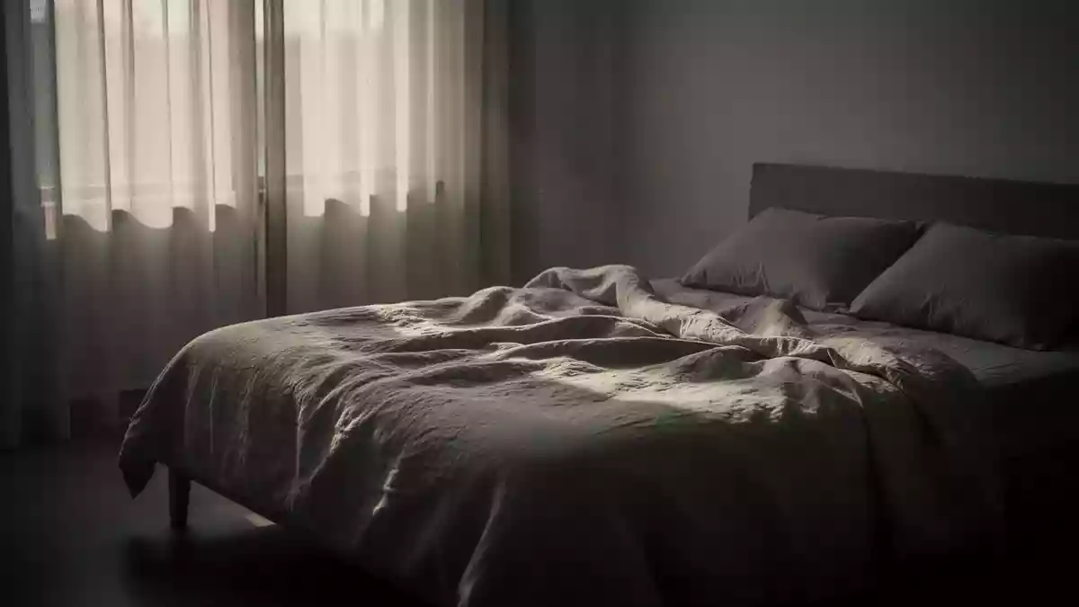 Ein minimalistisch eingerichtetes Schlafzimmer in den frühen Morgenstunden mit sanftem Licht und ungemachtem Bett. Illustration mit AI erstellt.