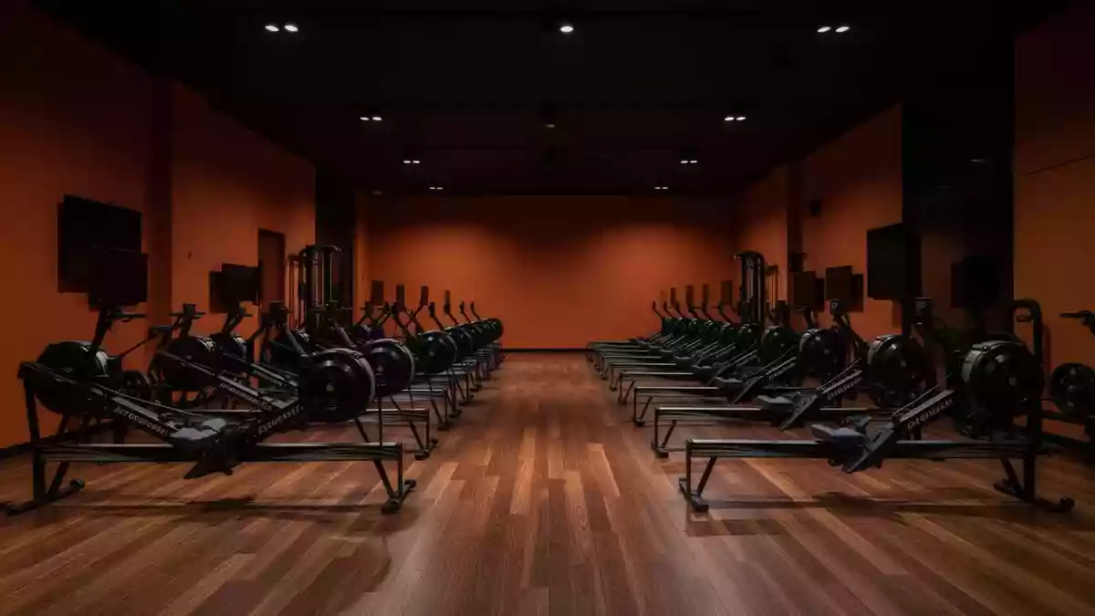 Ein minimalistisch gestalteter Fitnessraum mit dunklen, orangefarbenen Wänden und leeren Trainingsgeräten in einer Halle. Illustration mit AI erstellt.