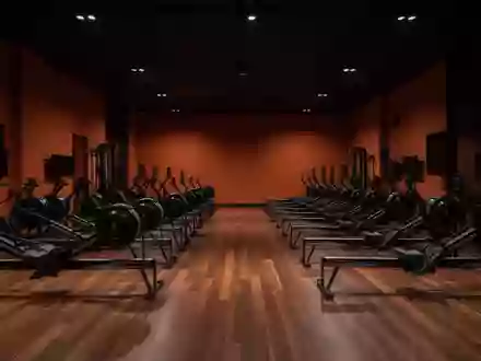 Ein minimalistisch gestalteter Fitnessraum mit dunklen, orangefarbenen Wänden und leeren Trainingsgeräten in einer Halle. - Foto: über boerse-global.de
