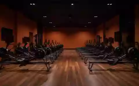 Ein minimalistisch gestalteter Fitnessraum mit dunklen, orangefarbenen Wänden und leeren Trainingsgeräten in einer Halle. - Foto: über boerse-global.de
