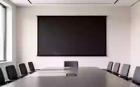 Ein minimalistischer Konferenzraum mit einer leeren, dunklen Projektionsfläche vor einer weißen Wand bei Tageslicht. - Foto: über boerse-global.de