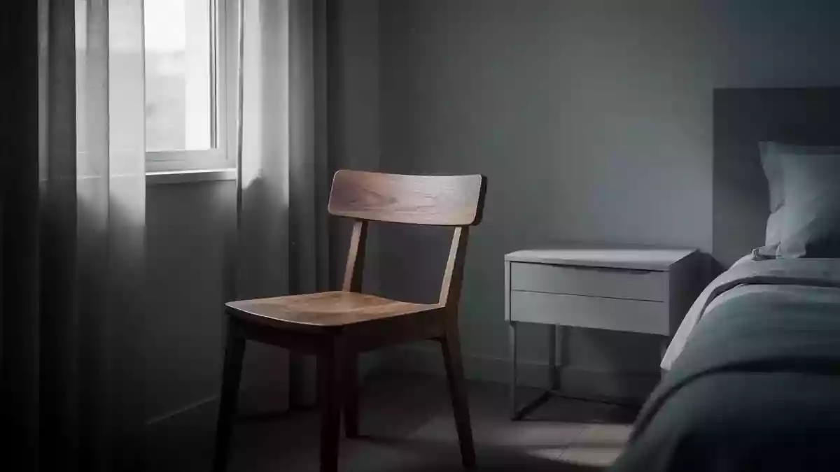 Ein ruhiger, schattiger Raum mit einem leeren Stuhl und einem Beistelltisch in gedämpftem Licht. Illustration mit AI erstellt.