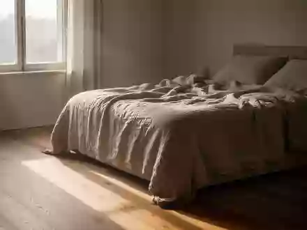 Sonnenlicht fällt in einem minimalistischen Schlafzimmer auf den Holzboden neben einem ungemachten Bett. - Foto: über boerse-global.de