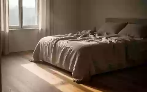 Sonnenlicht fällt in einem minimalistischen Schlafzimmer auf den Holzboden neben einem ungemachten Bett. - Foto: über boerse-global.de